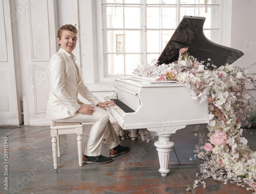 young man teenager in a white business suit with a large white piano in flowers. caucasian male play music at holiday alone.