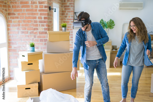 Young couple moving to a new house having fun playing with virtual reality glasses around cardboard boxes © Krakenimages.com