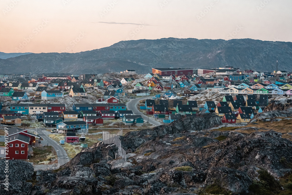 Aerial View of Arctic city of Ilulissat, Greenland during sunrise sunset with fog. Colorful houses in the center of the town with icebergs in the background in summer on a sunny day with orange pink