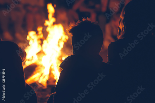 Boys and girls sitting near campfire and talking.