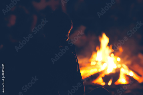 Boy with friends sitting near campfire and looking at the flame.