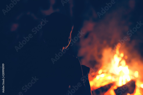 Boy with friends sitting near campfire and looking at the flame.