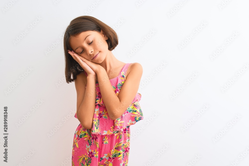 Young beautiful child girl wearing pink floral dress standing over isolated white background sleeping tired dreaming and posing with hands together while smiling with closed eyes. Young beautiful child girl wearing pink floral dress standing over isolated white background sleeping tired dreaming and posing with hands together while smiling with closed eyes.