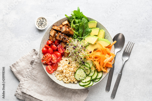 Trendy colorful vegan buddha bowl salad with fried tofu, carrot, cucumber, bulgur avocado tomato and green salad leaf on grey concrete background. Top view. Balanced diet food photo