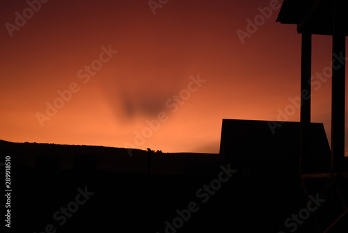 Bright orange cloudless sky with a black silhouette of a wooden building with copyspace area for late evening or romantic based designs and ideas