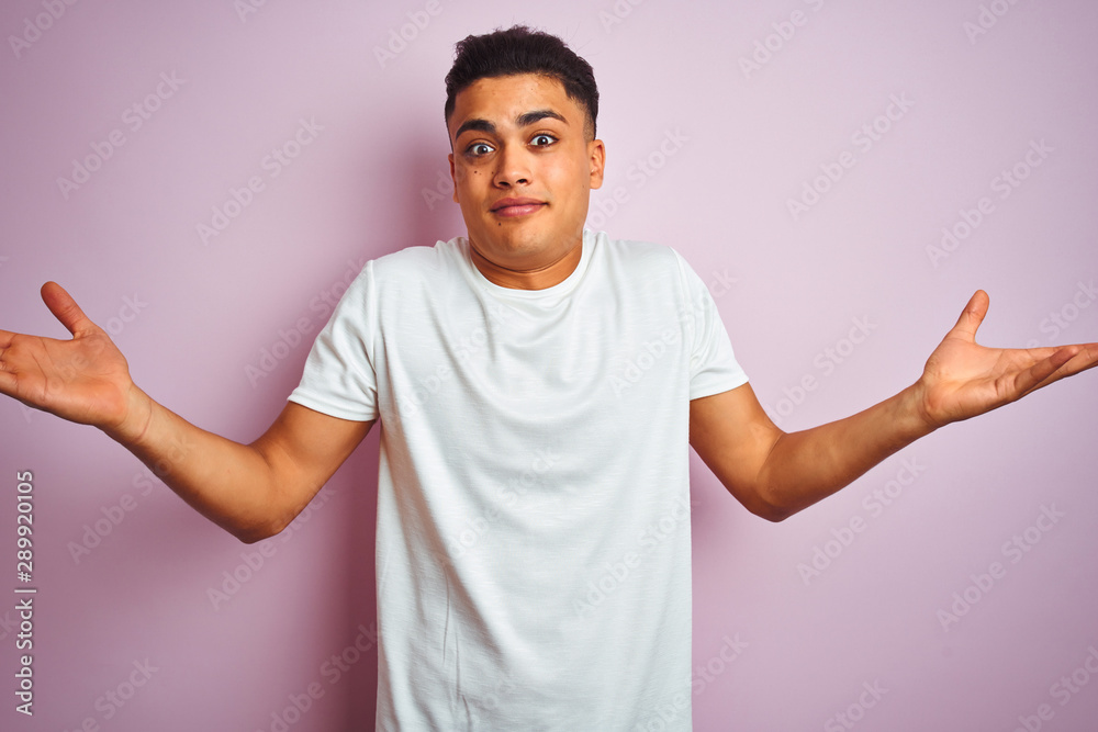 Young brazilian man wearing t-shirt standing over isolated pink background clueless and confused expression with arms and hands raised. Doubt concept. Young brazilian man wearing t-shirt standing over isolated pink background clueless and confused expression with arms and hands raised. Doubt concept.