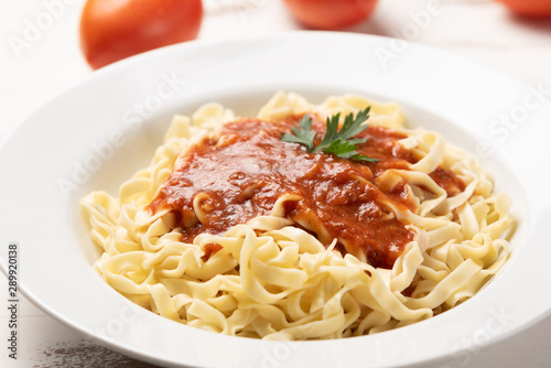 Fettuccine pasta with tomato sauce, parsley and basil in a white plate on a rustic wooden table background, soft light
