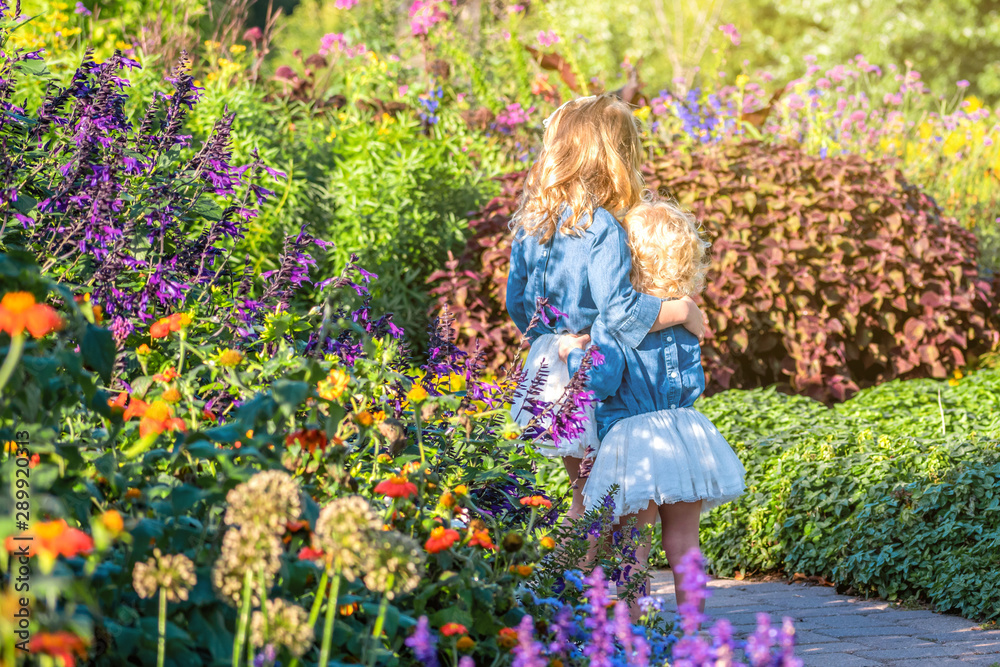 Two young girls with blond hair are enjoying a flower garden Two young girls with blond hair are enjoying a flower garden