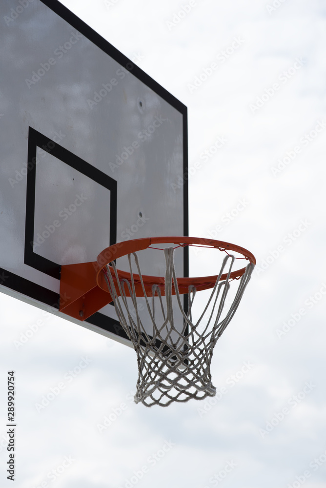 Basketball hoop, basket with white net and blue sky with clouds in background