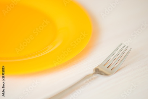 orange plate and fork closeup on the light wooden table.
