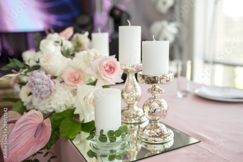 Fototapeta Naklejka Na Ścianę i Meble -  The wedding table setting for the newlyweds is decorated with fresh flowers of carnation, rose, anthurium and eucalyptus leaves. Silver candlesticks, white candles. Wedding floristry. Closeup details