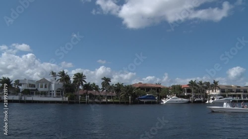 Boat Passing Right to Left in Front of Luxury Homes on the Intracoastal Waterway of the Pompano Inlet Hillsboro Mile in a Sunny Spring Afternoon, Blue Sky with Scattered Clouds