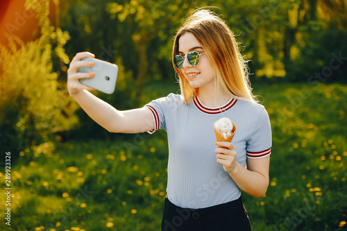 beautiful young beautiful girl with shiny blond hair and a skirt spend goood time in a sunny summer park with ice cream and use the phone photo