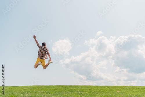 back view of boy with outstretched hand jumping against blue sky