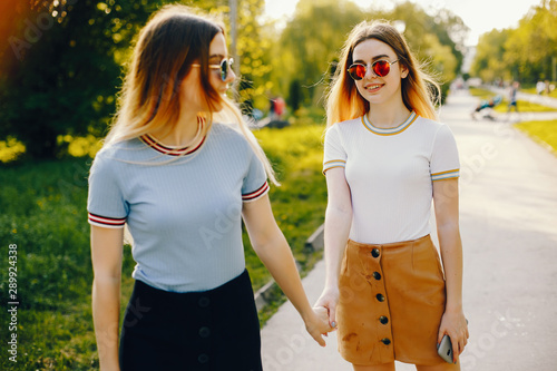 two beautiful young beautiful girls with shiny blond hair and a skirt and walk and spend goood time in a sunny summer park photo