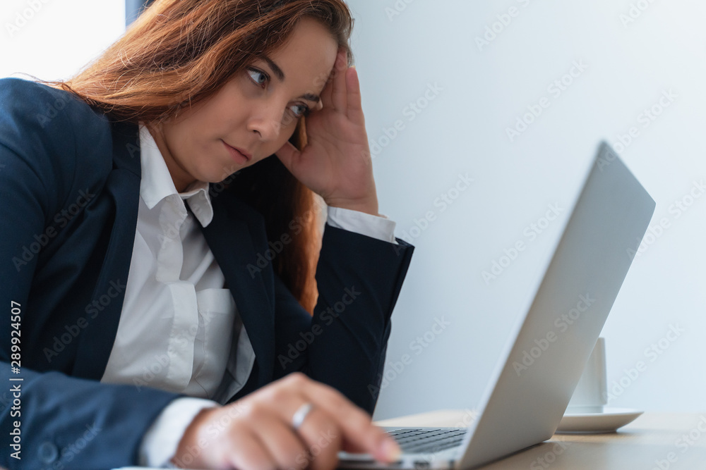 Tired and stressed young woman looks at laptop screen in office. Overworked person with headache Tired and stressed young woman looks at laptop screen in office. Overworked person with headache