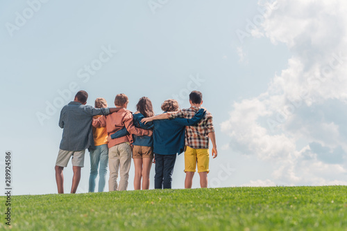 selective focus of multicultural kids standing and hugging in park photo