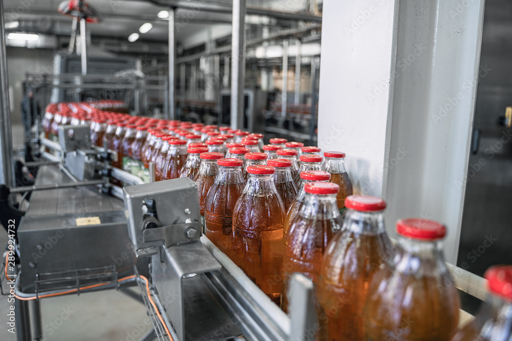 Conveyor belt or line in beverage factory or plant interior inside with modern industrial machine equipment. Bottles with fresh organic juice