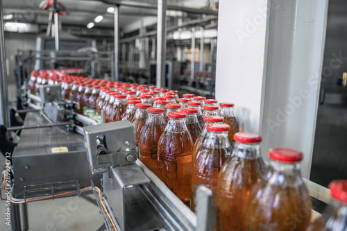 Conveyor belt or line in beverage factory or plant interior inside with modern industrial machine equipment. Bottles with fresh organic juice