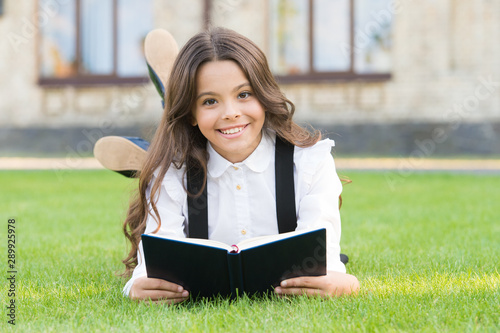 Basic education. Extracurricular reading. Cute small child reading book outdoors. Adorable little girl learn reading. Schoolgirl school uniform laying on lawn with favorite book. Studying concept