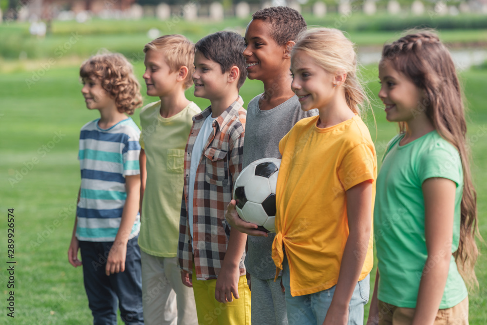 Obraz premium selective focus of happy multicultural kids standing on grass with football
