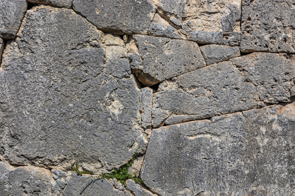 The ancient megalithic walls surround the acropolis of Amelia, in Umbria, Italy. Texture composed ofirregular huge blocks of stone. The grass grows between the interstices of the wall. The ancient megalithic walls surround the acropolis of Amelia, in Umbria, Italy. Texture composed ofirregular huge blocks of stone. The grass grows between the interstices of the wall.
