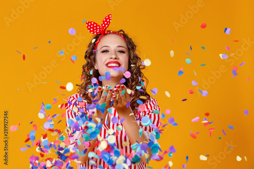 cheerful funny young woman with festive confetti on yellow