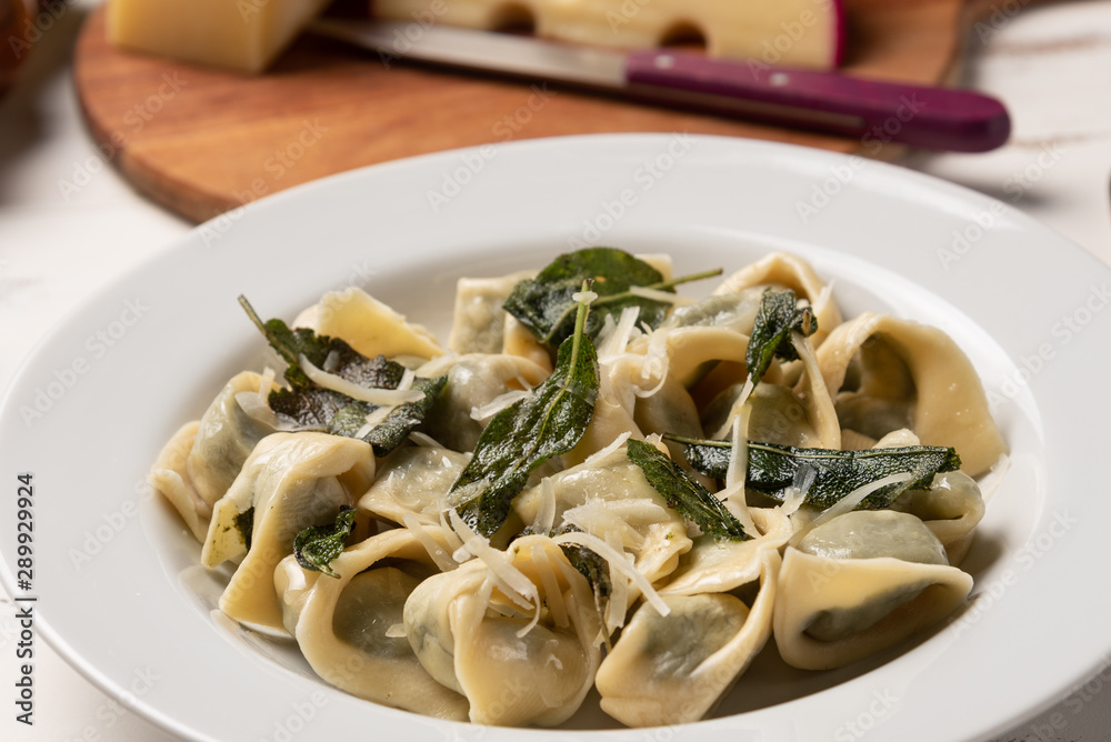 Homemade tortellini with butter and sage in a white plate on white wooden table background. Soft light Homemade tortellini with butter and sage in a white plate on white wooden table background. Soft light