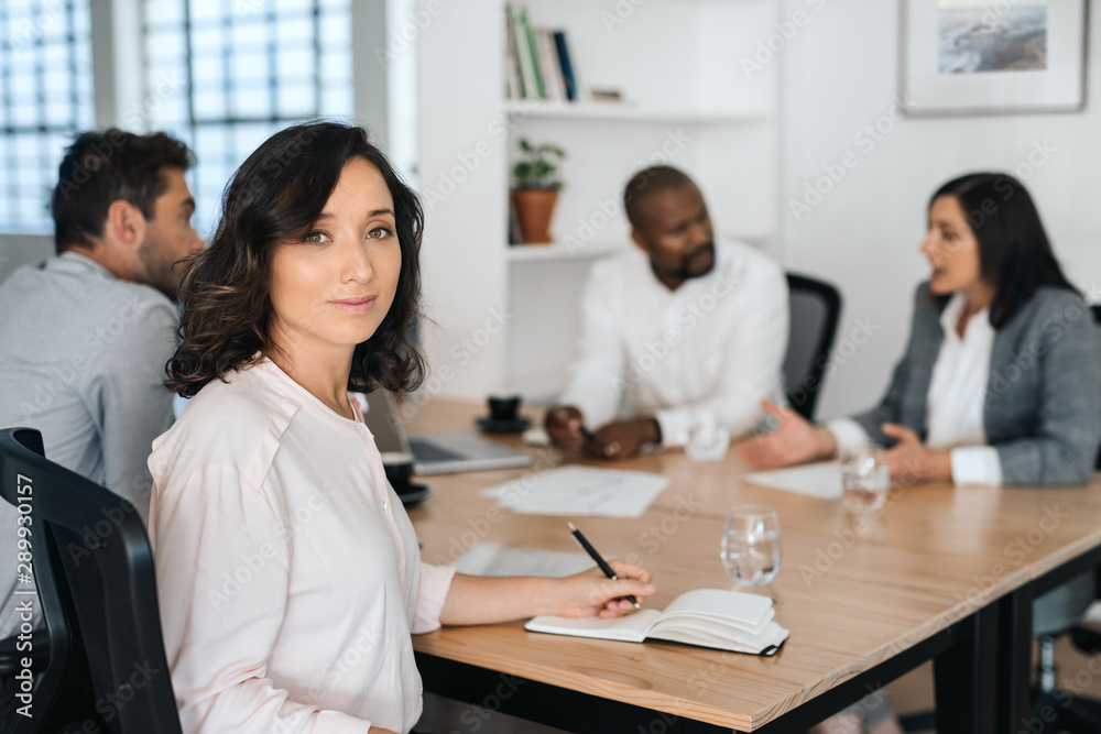 Smiling young businesswoman sitting with colleagues in a boardroom