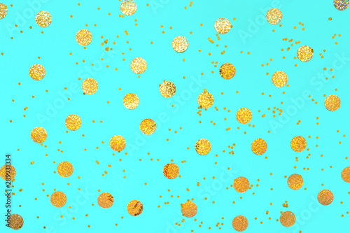 Photo of gold confetti sprinkles in different sizes on pastel cyan backdrop. Christmas pattern. Festive holiday background. for your projects. Celebration concept. Top view, flat lay