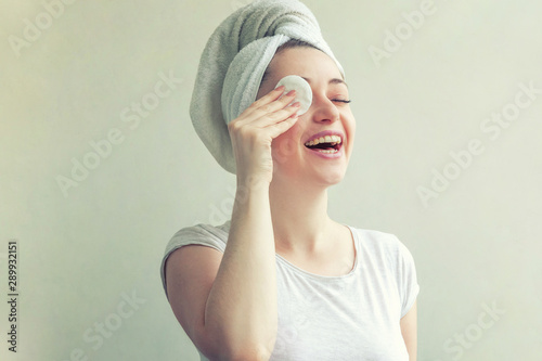 Beauty portrait of smiling woman in towel on head with soft healthy skin removing make up with cotton pad isolated on white background. Skincare cleansing spa relax concept