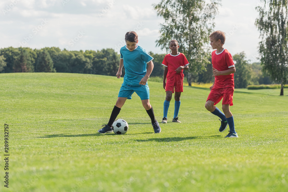 Obraz premium cute multicultural friends playing football on green grass