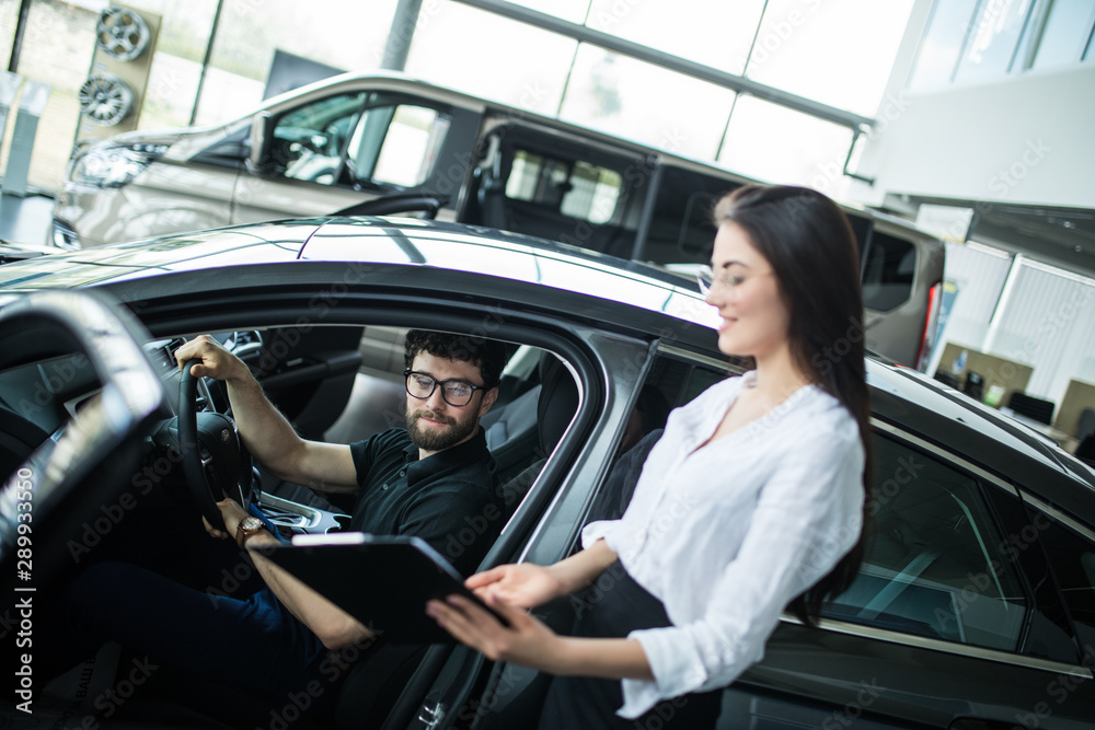 Young woman Manager showing something on a clipboard to the customer in car showroom Young woman Manager showing something on a clipboard to the customer in car showroom