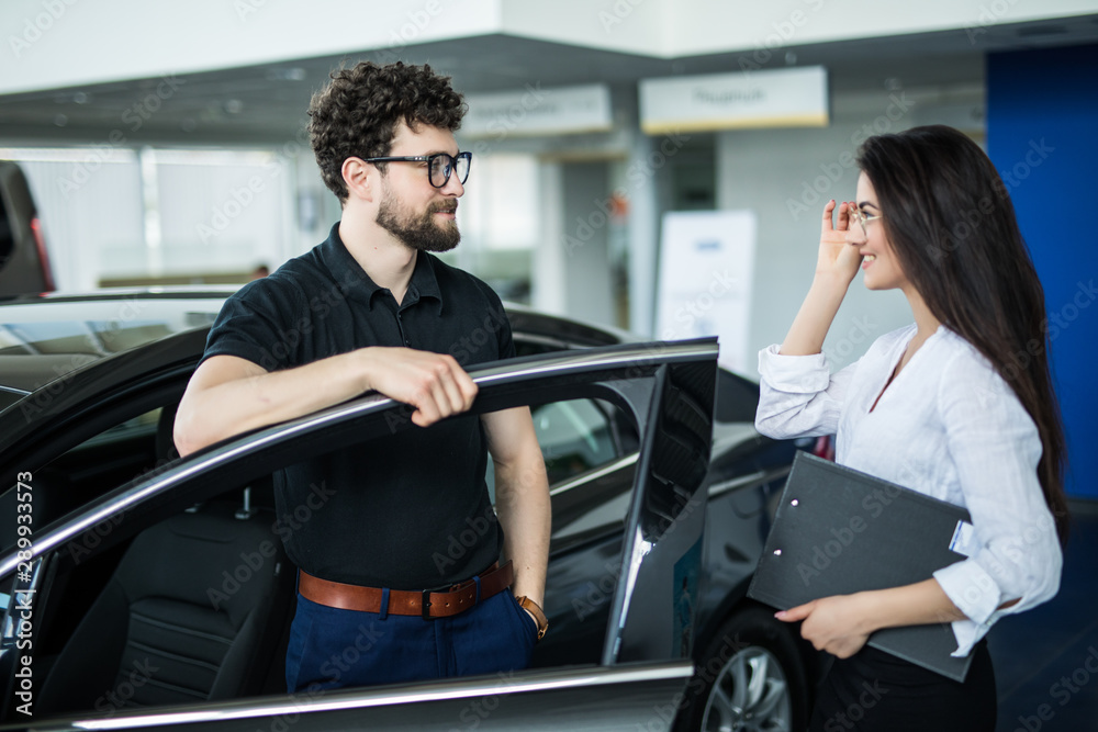 Young woman Manager showing something on a clipboard to the customer in car showroom Young woman Manager showing something on a clipboard to the customer in car showroom