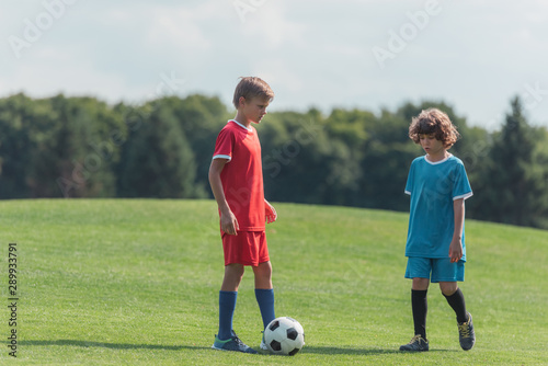 cute curly boy playing football with friend on grass in park