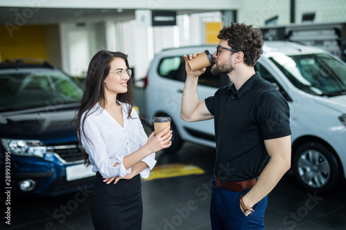 Sales manager describing car to customer in showroom while drinking coffee