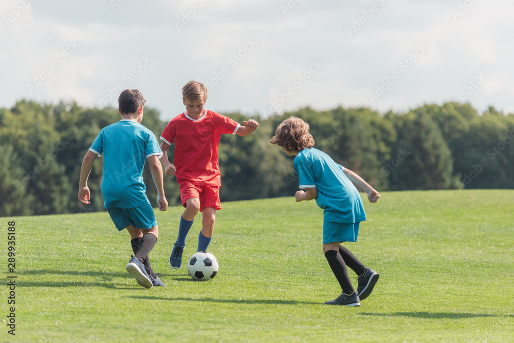 curly boy playing football with friends on green grass