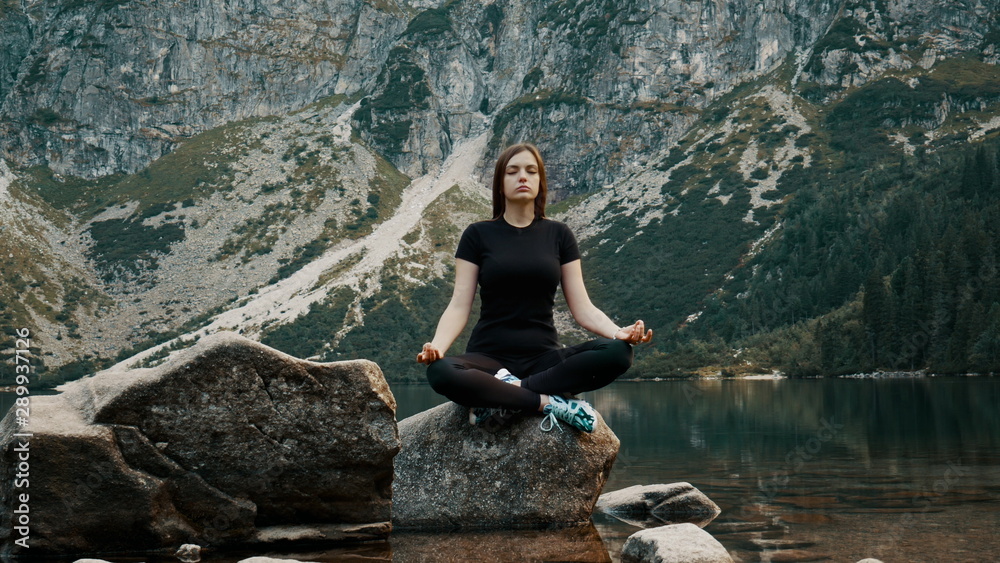 Beautiful and healthy young woman meditates on a mountain lake, practicing yoga at evening, enjoys the tranquility high in the mountains