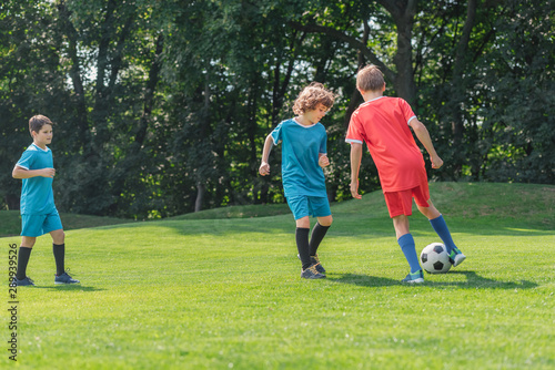cute curly boy playing football with friends on grass