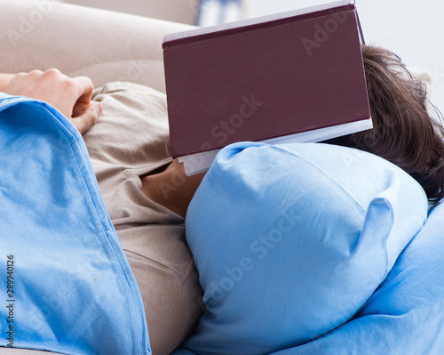 Young student man preparing for college exams in bed with book