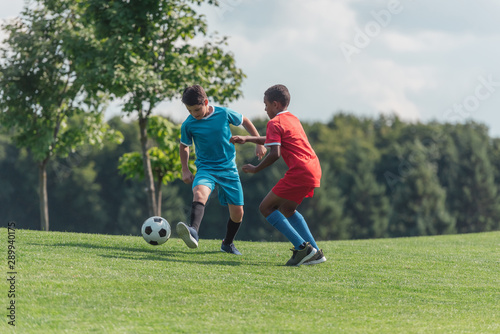 cute multicultural children playing football on grass