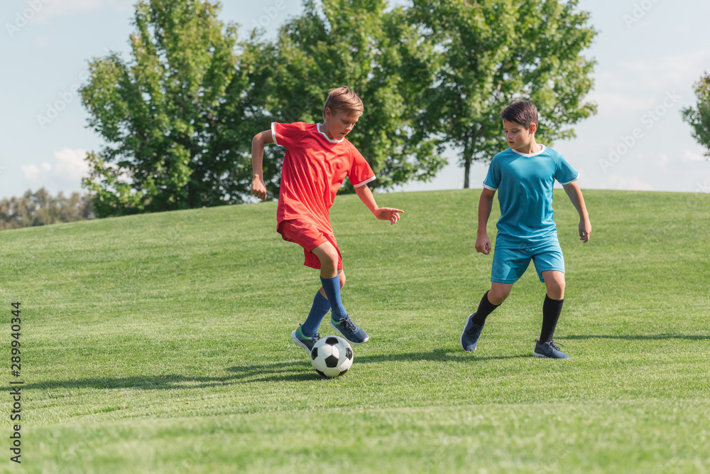 cute friends in sportswear playing football on green grass in park cute friends in sportswear playing football on green grass in park