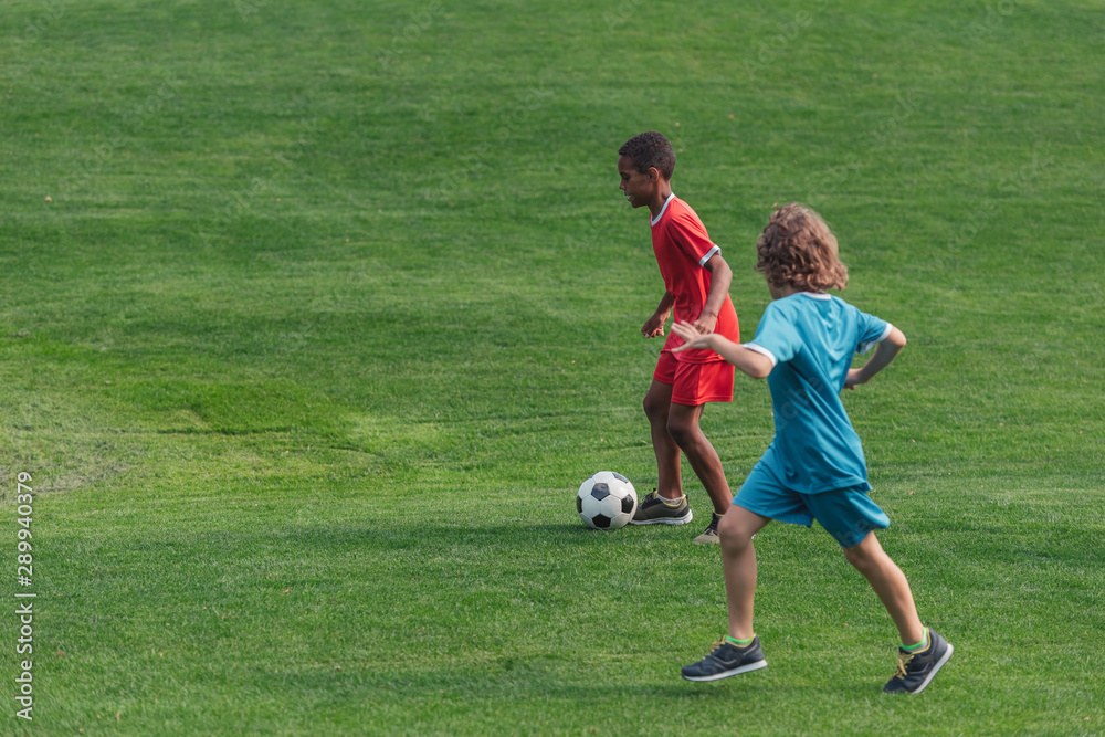 cute multicultural kids playing football on grass cute multicultural kids playing football on grass