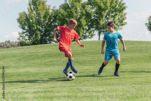 cute friends in sportswear playing football on green grass in park © LIGHTFIELD STUDIOS