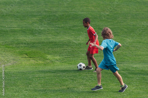 cute multicultural kids playing football on grass