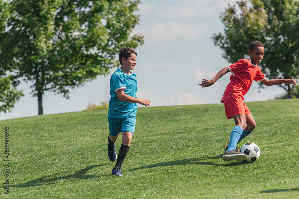 adorable multicultural children playing football on green grass adorable multicultural children playing football on green grass