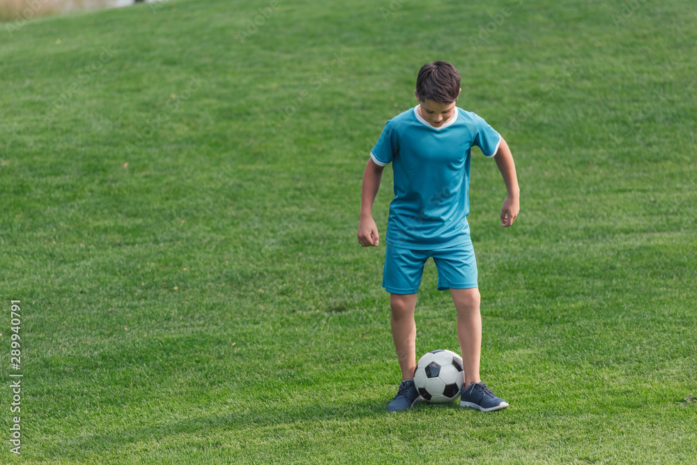 kid in sportswear standing on green grass with football