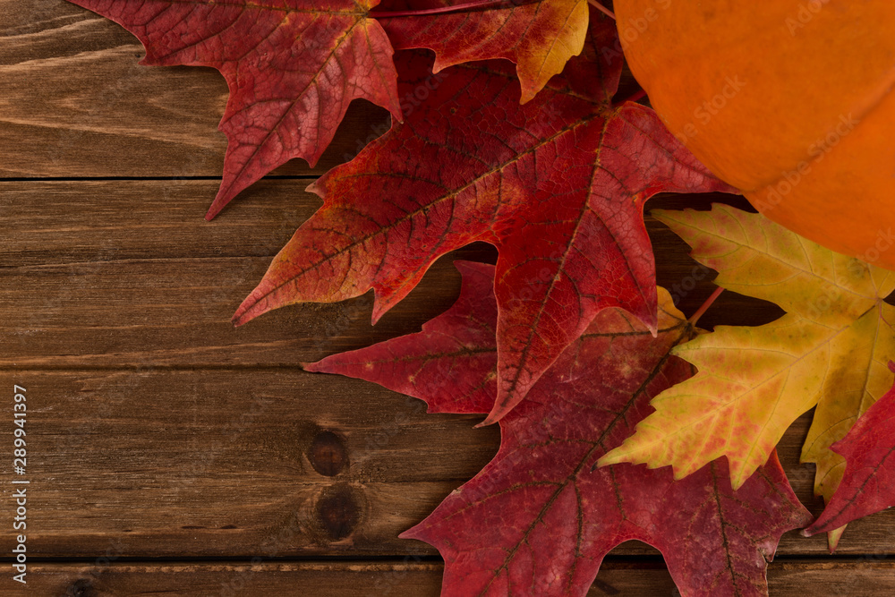 Pumpkin with red maple leafs disposed on a wooden table. Flat lay, top view of fall autumn concept.