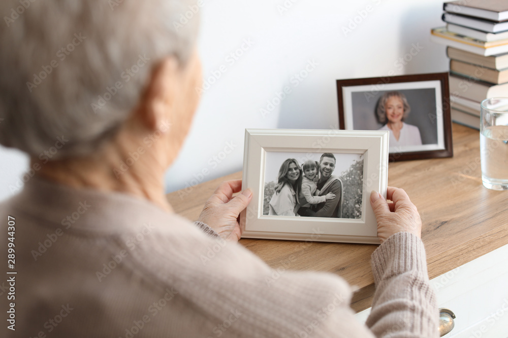 Elderly woman with framed family portrait at home - obrazy, fototapety, plakaty 