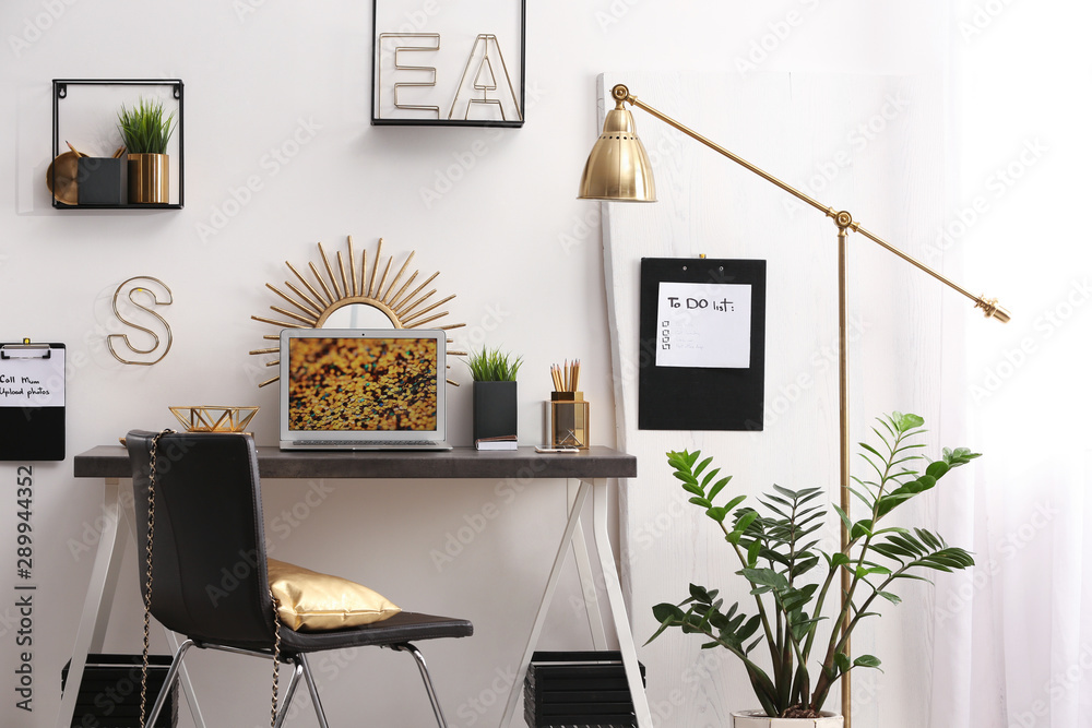 Modern workplace with laptop and golden decor on desk near wall. Stylish interior design - obrazy, fototapety, plakaty 